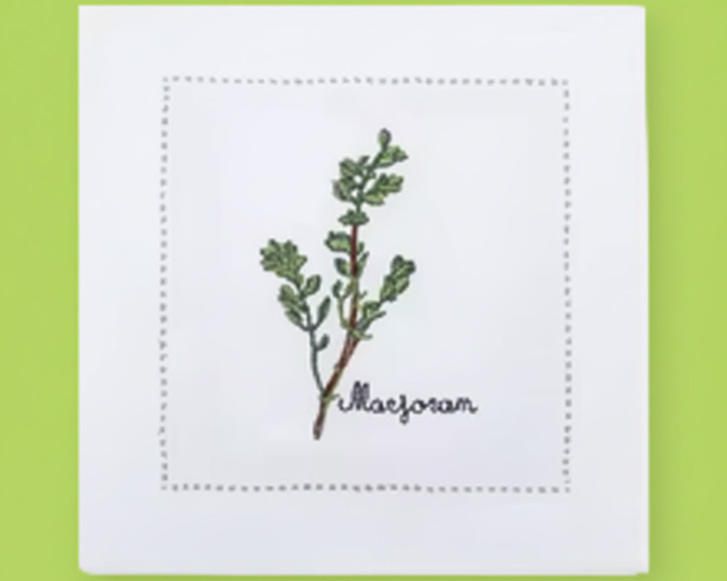 Single white linen cocktail napkin featuring a detailed green Marjoram branch embroidery with a decorative hemstitch perimeter.