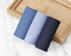 Three folded towels in blue and gray on a wooden tray with a marble background