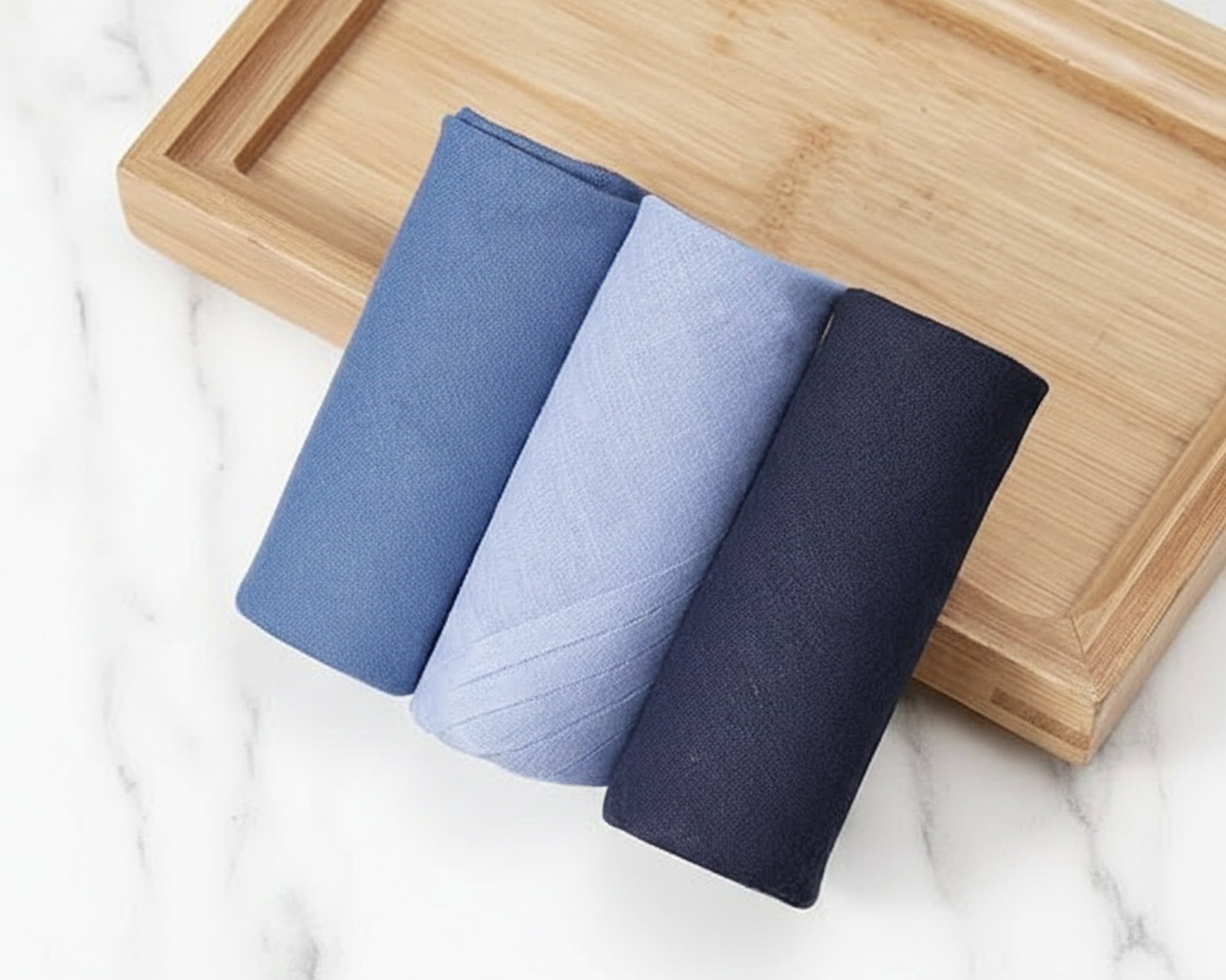 Three folded towels in blue and gray on a wooden tray with a marble background
