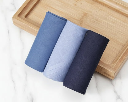 Three folded towels in blue and gray on a wooden tray with a marble background