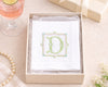 Boxed set with a card featuring a decorative letter 'D' on a table with a glass of pink drink and pearl necklace.