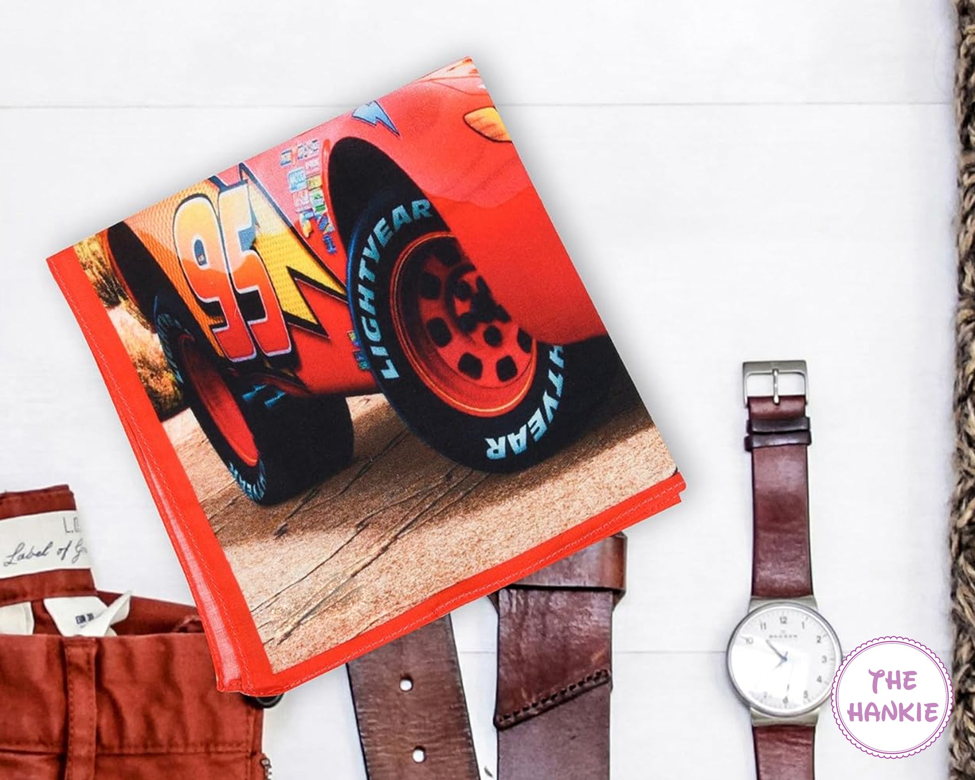 Book with a car tire design on a white surface, next to a watch and brown pants.