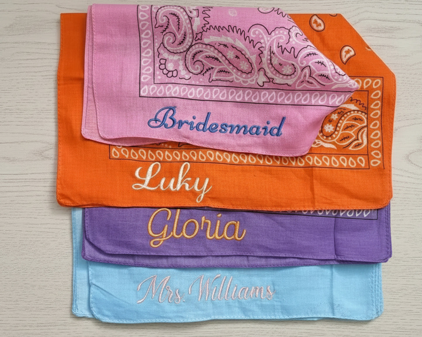 Close-up flat lay of personalized "Mrs. Williams" and "Bridesmaid" bandanas on a light wood background with tropical shadows.