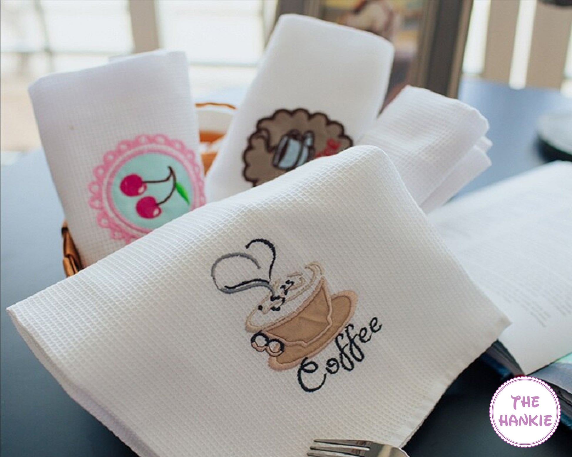 White hankies with embroidered designs on a table, featuring the brand 'The Hankie'.