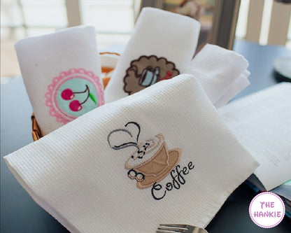 White hankies with embroidered designs on a table, featuring the brand 'The Hankie'.