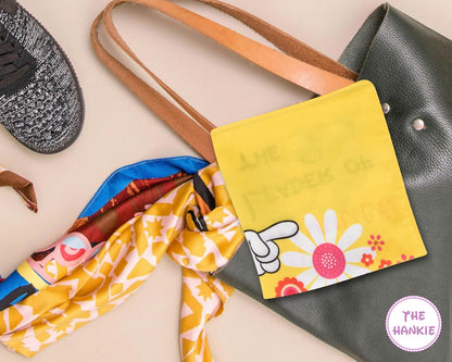 Colorful hankie with a floral design and text, attached to a black handbag.