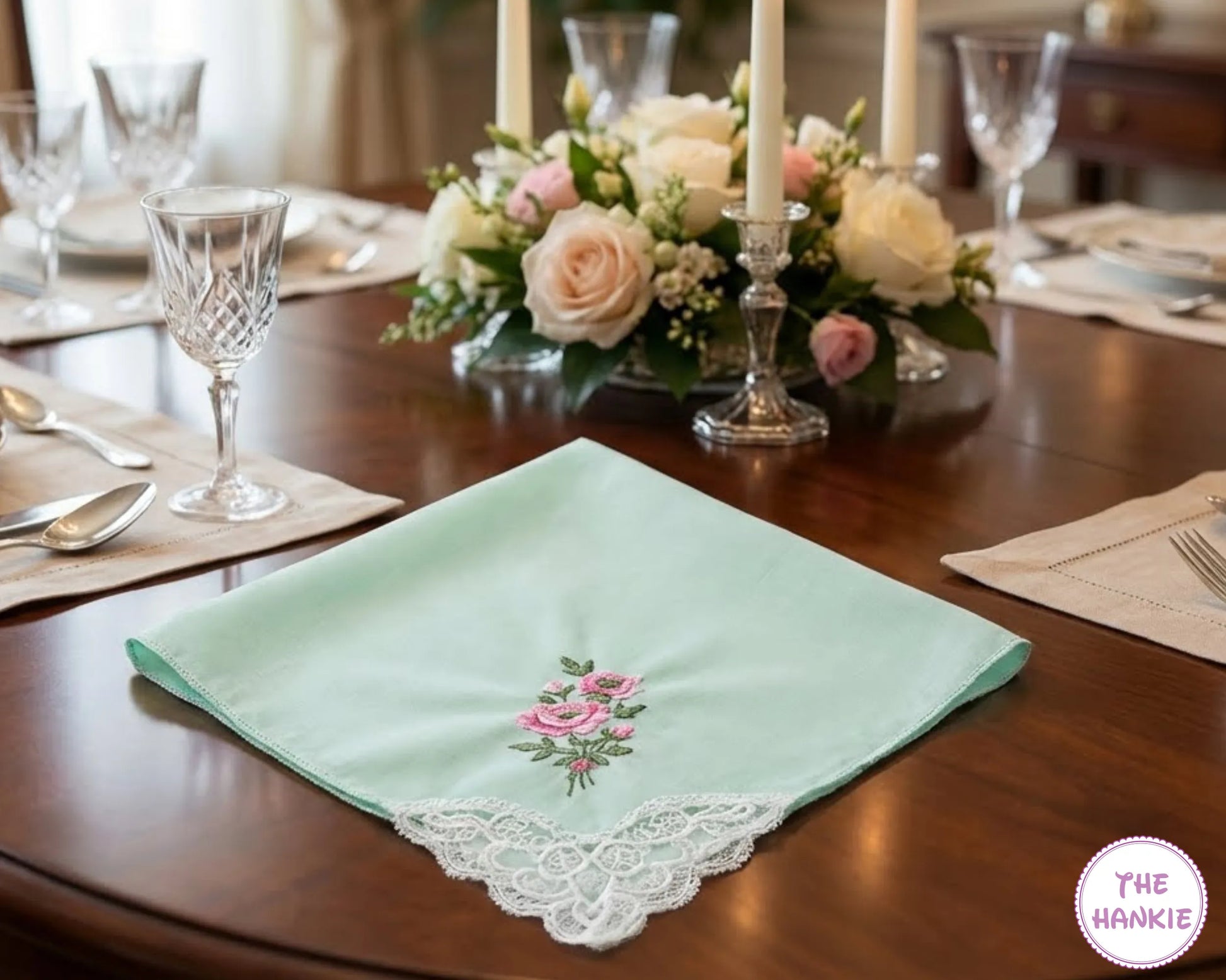 Decorative green hankie with floral embroidery on a table setting with flowers and glasses.