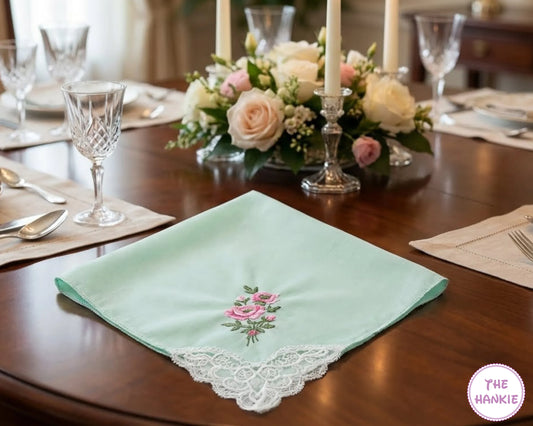 Decorative green hankie with floral embroidery on a table setting with flowers and glasses.