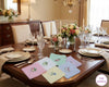 Dining table set with floral hanky, glasses, and cutlery in a well-decorated room.