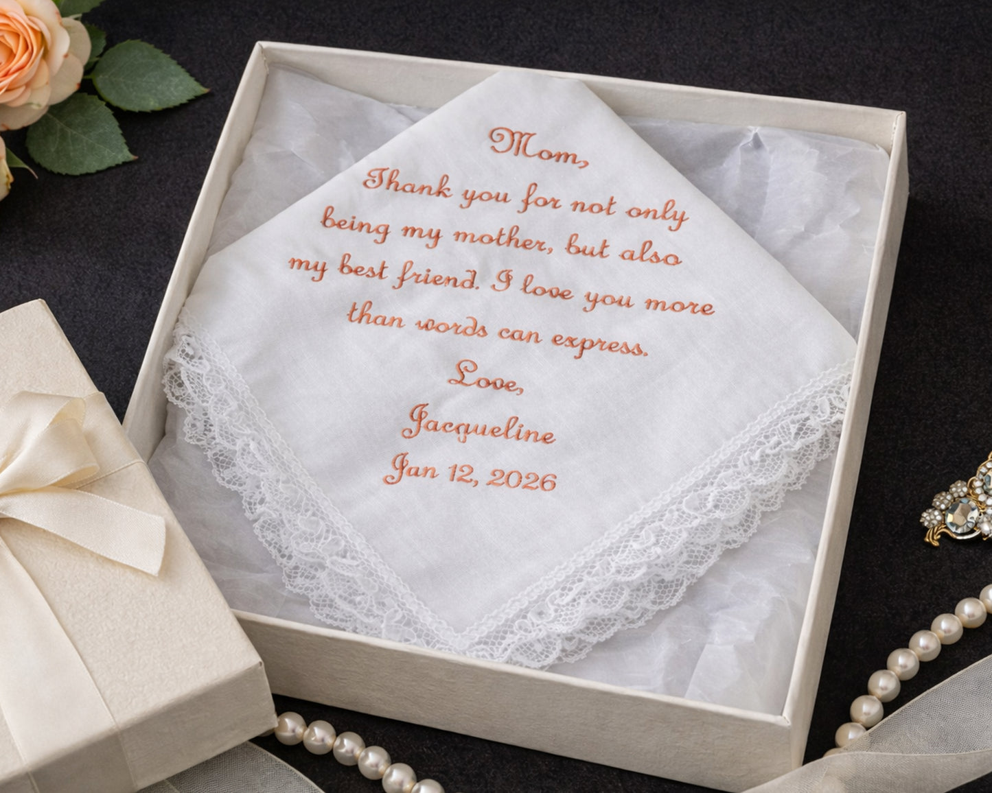 Embroidered handkerchief in a box with personalized message, surrounded by decorative items.