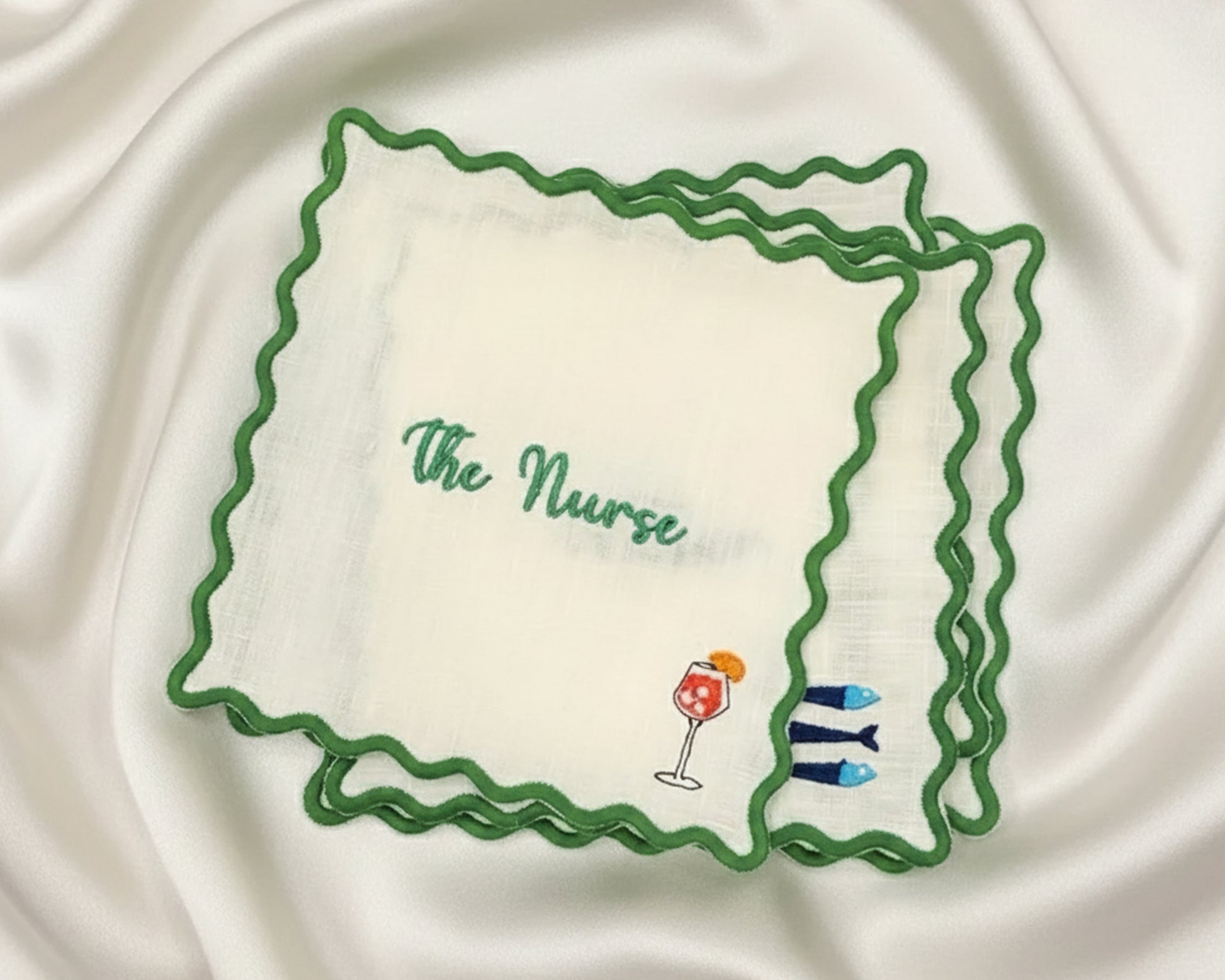 Embroidered handkerchief with 'The Nurse' text and drink illustrations on a satin background