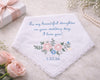 Embroidered handkerchief with floral design and personalized text on a marble surface with flowers and a gift box.