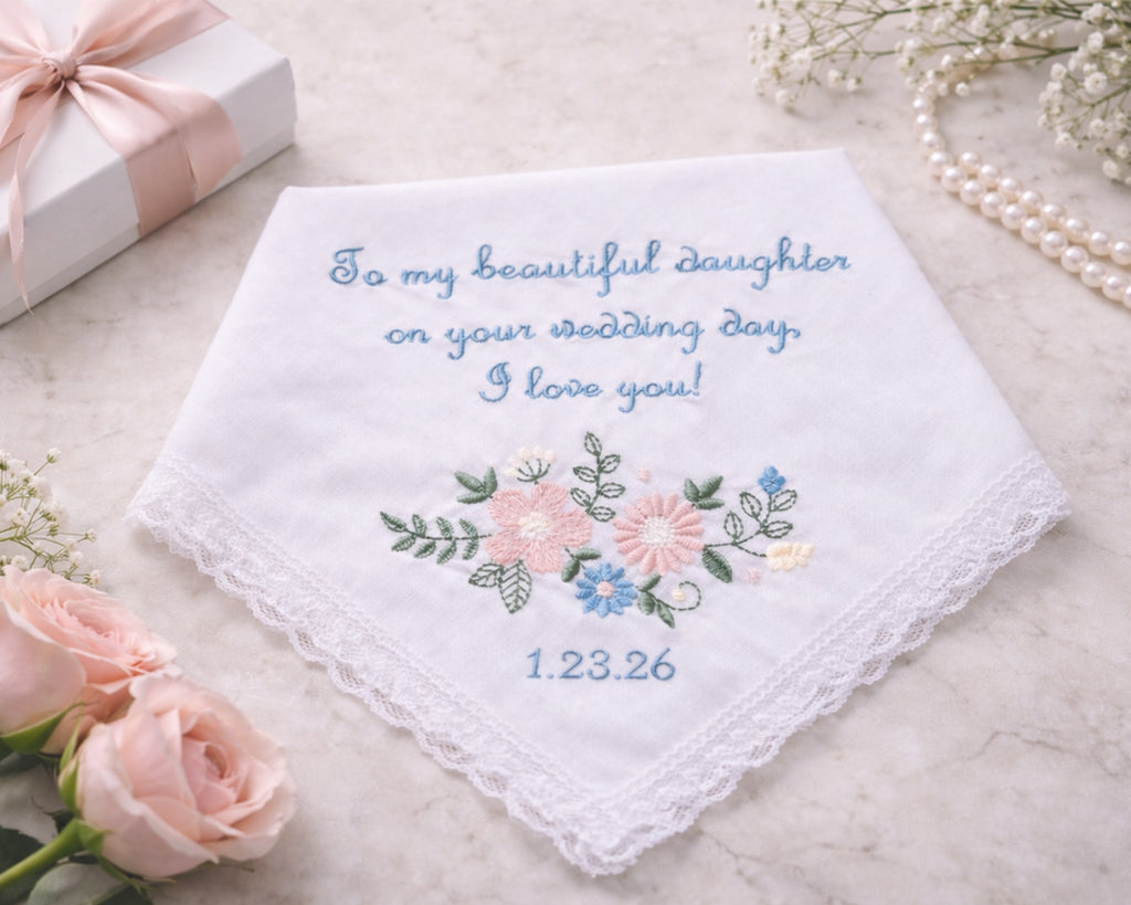 Embroidered handkerchief with floral design and personalized text on a marble surface with flowers and a gift box.