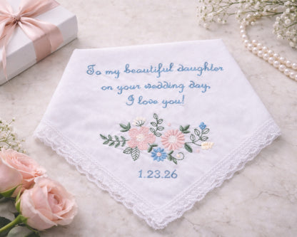 Embroidered handkerchief with floral design and personalized text on a marble surface with flowers and a gift box.