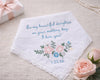 Embroidered wedding handkerchief with floral design and text on a beige surface with roses and a gift box.