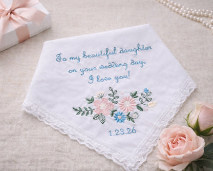 Embroidered wedding handkerchief with floral design and text on a beige surface with roses and a gift box.