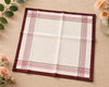 Folded checkered hanky with red and white stripes on a beige surface with flowers and leaves.