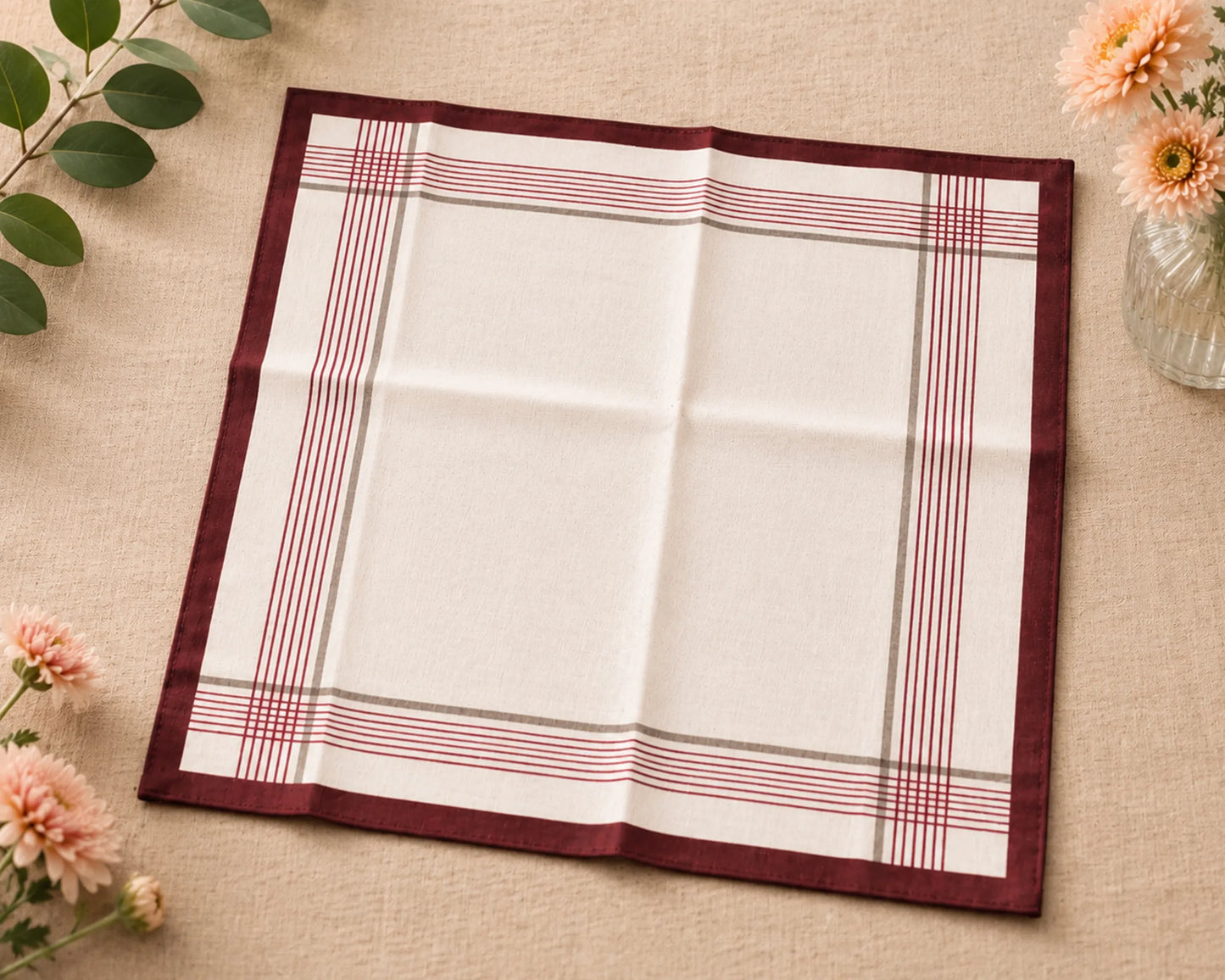 Folded checkered hanky with red and white stripes on a beige surface with flowers and leaves.
