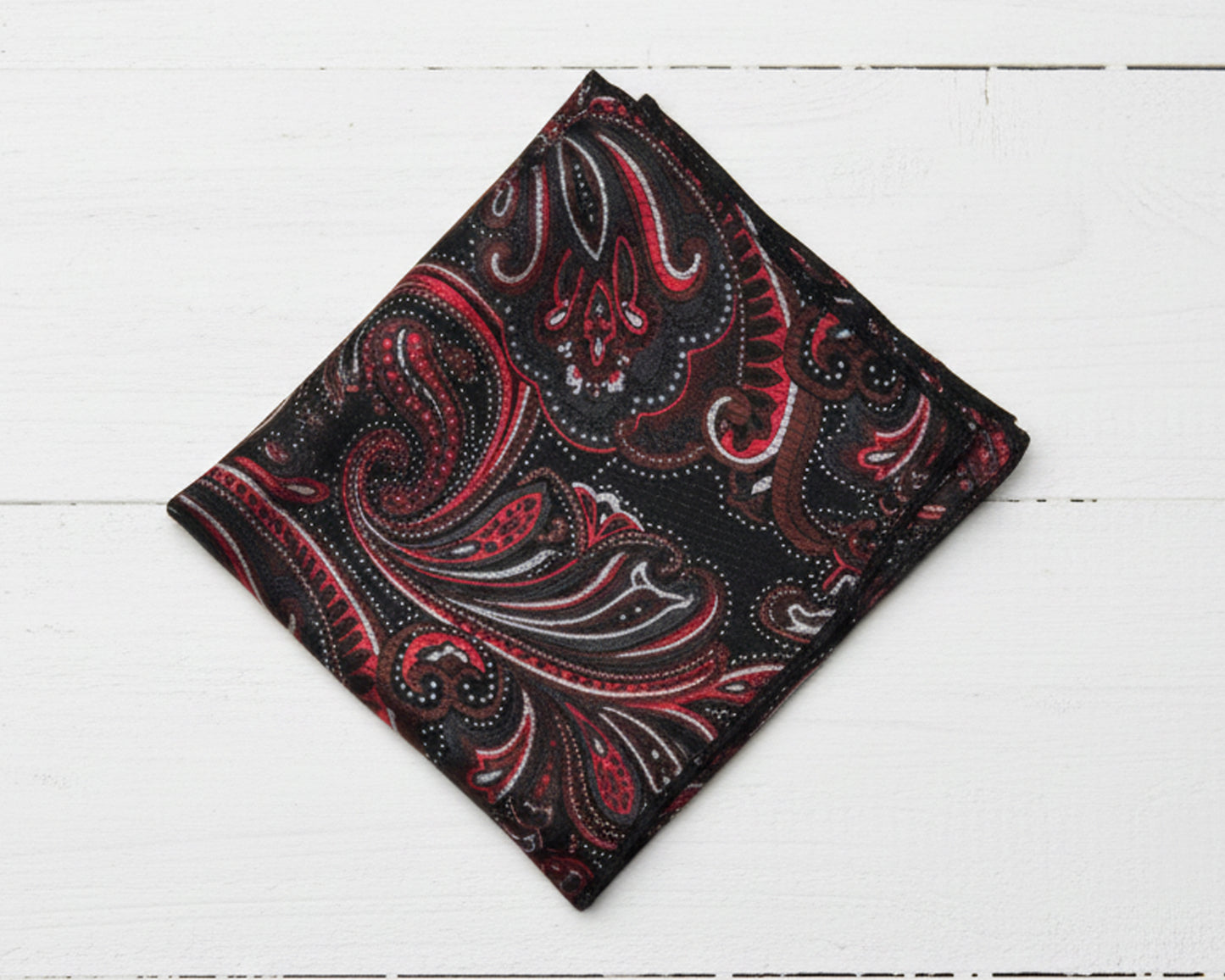 Folded red and black paisley patterned fabric on a white wooden surface