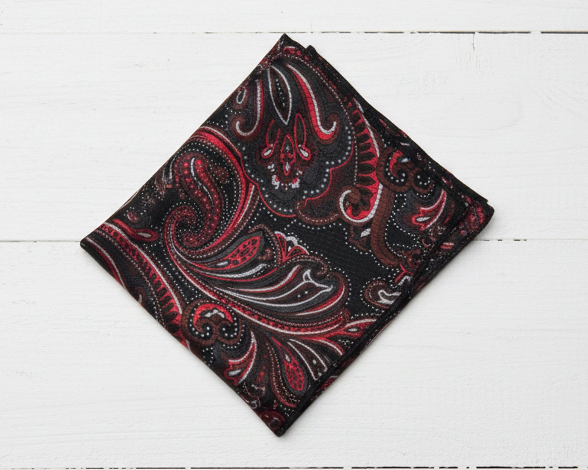 Folded red and black paisley patterned fabric on a white wooden surface