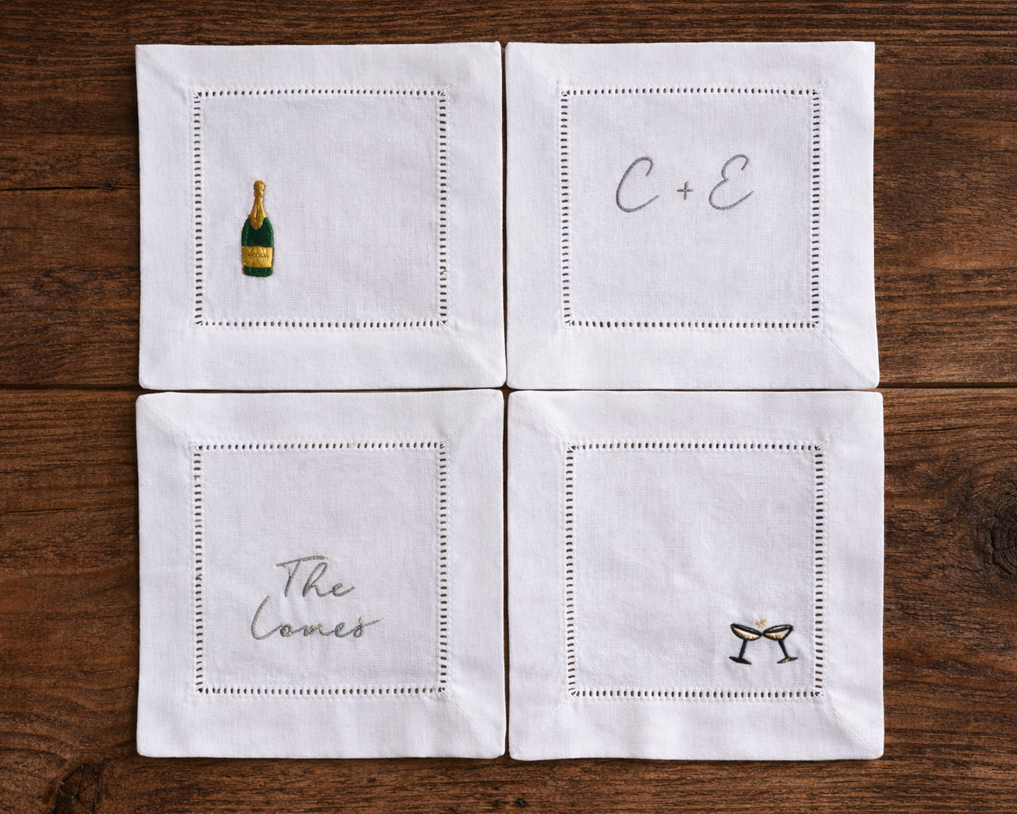 Four white cocktail napkins with embroidered designs on a wooden surface