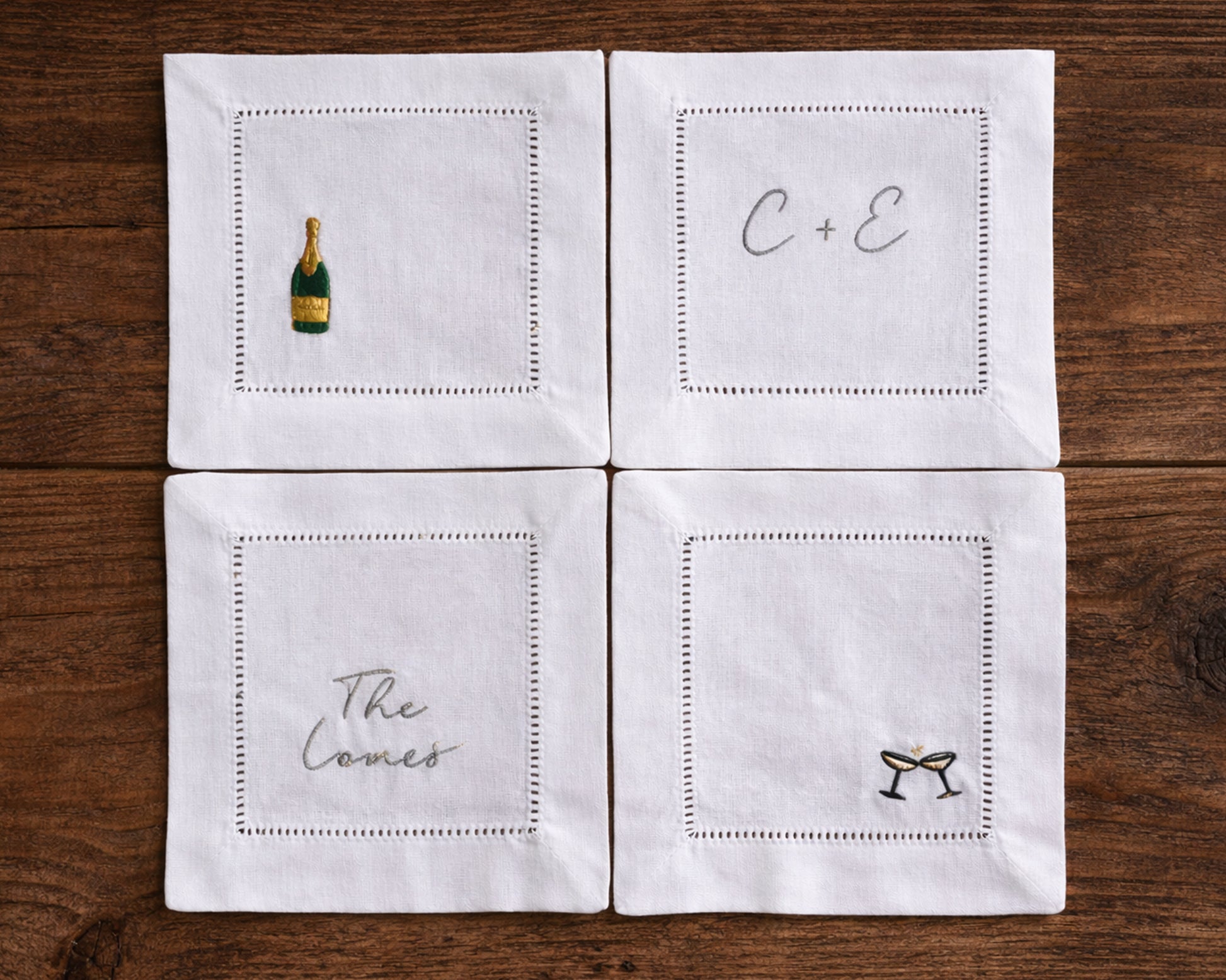 Four white cocktail napkins with embroidered designs on a wooden surface