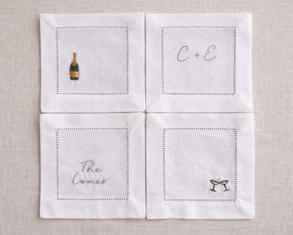 Four white napkins with embroidered designs on a beige background