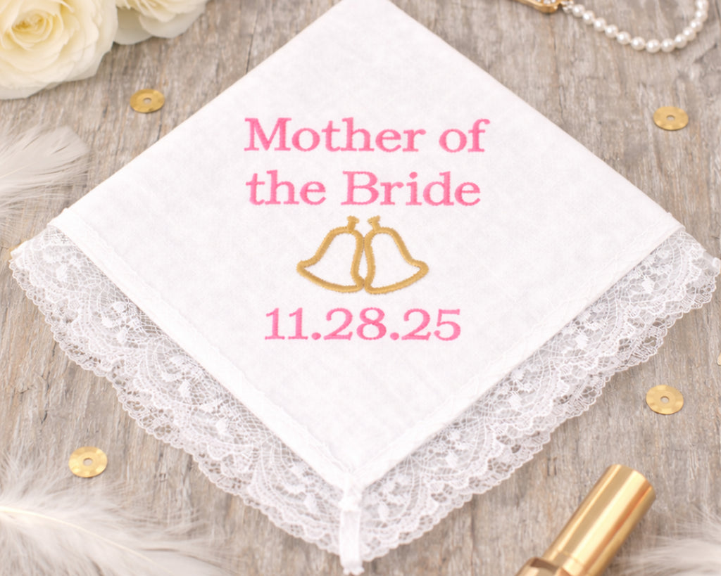 Handkerchief with 'Mother of the Bride' and wedding date on a wooden surface with flowers and jewelry.