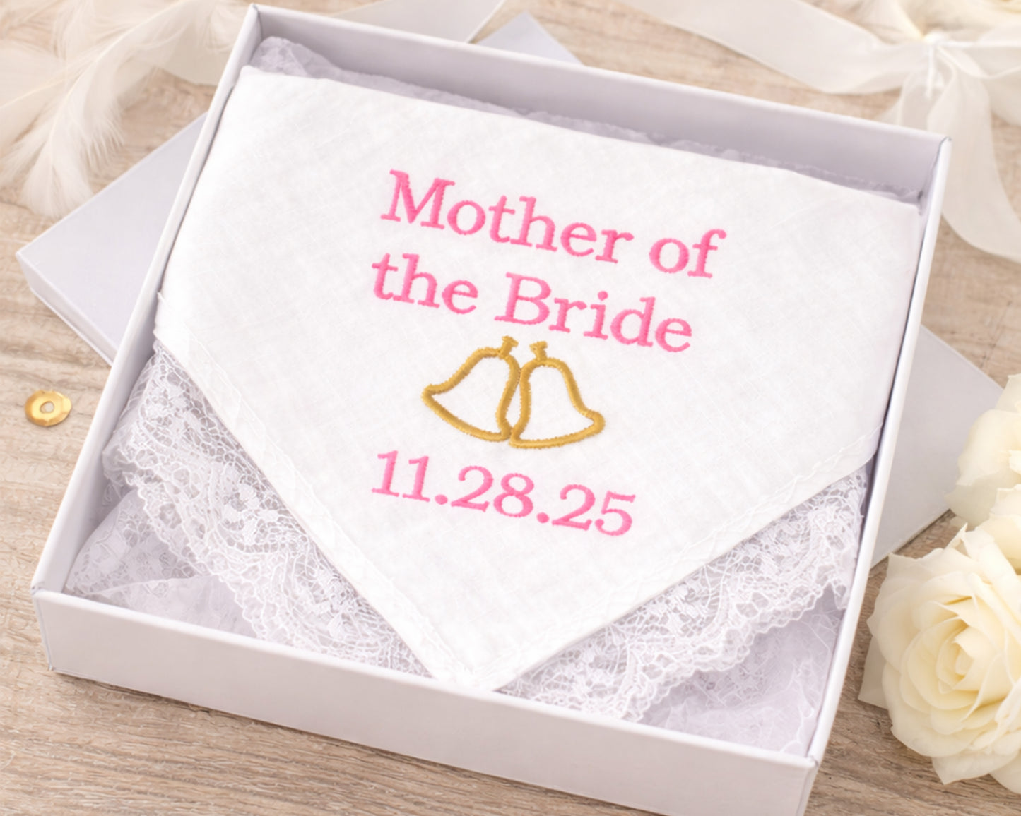 Handkerchief with 'Mother of the Bride' and wedding date embroidery in a box on a wooden surface.