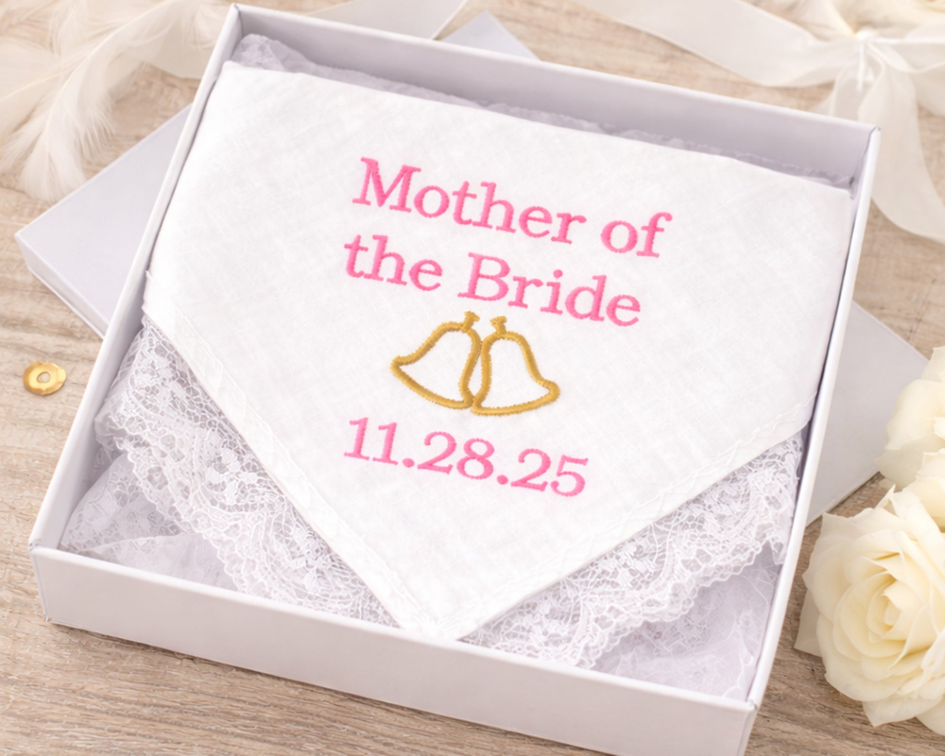 Handkerchief with 'Mother of the Bride' and wedding date embroidery in a box on a wooden surface.