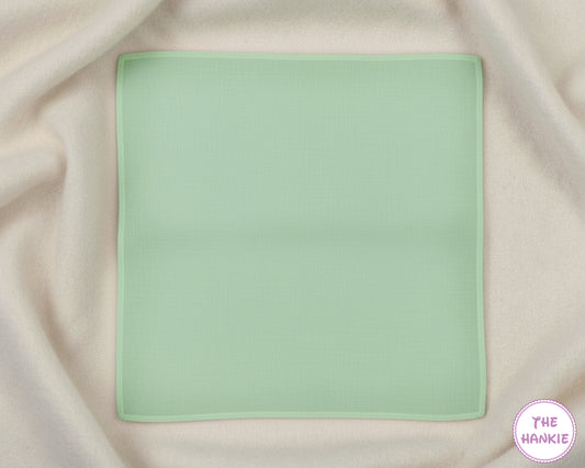 Light green handkerchief on a beige fabric background with 'The Hankie' brand logo.