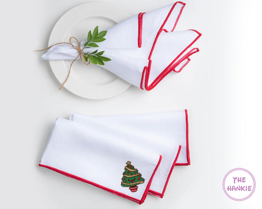 Two white hankies with red trim on a white plate, one featuring a Christmas tree design.