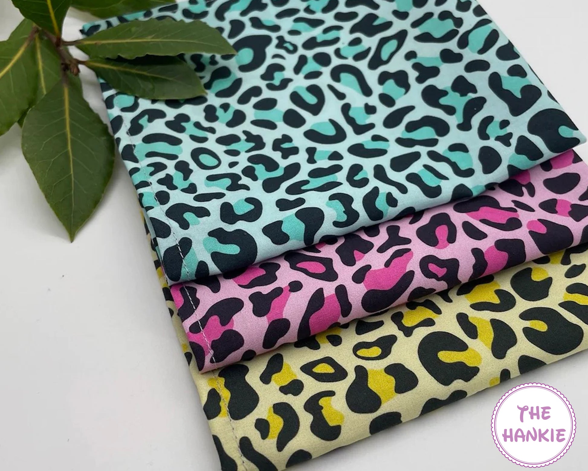 Three fabric hankies with leopard print patterns on a white surface, branded 'The Hankie'.