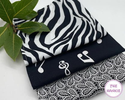 Three black and white patterned hankies on a white surface with a leafy branch.