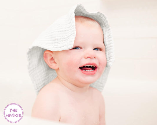 Baby wearing a white hooded towel with 'The Hankie' logo.