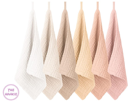 Set of five soft, textured towels in various pastel colors hanging against a white background.