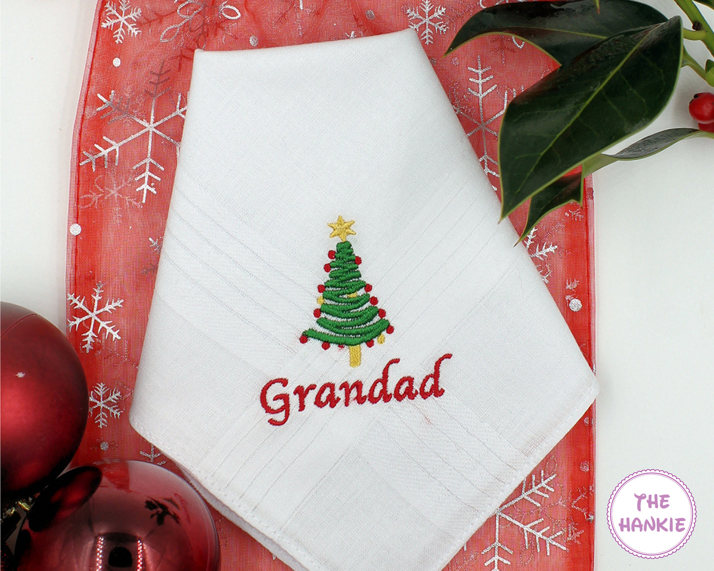 White handkerchief with embroidered Christmas tree and 'Grandad' text on a red decorative background.