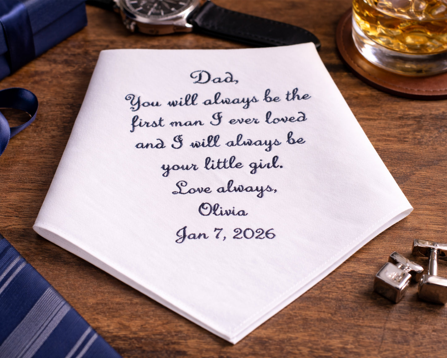 Personalized handkerchief with a message to a father on a wooden surface with a glass of whiskey.