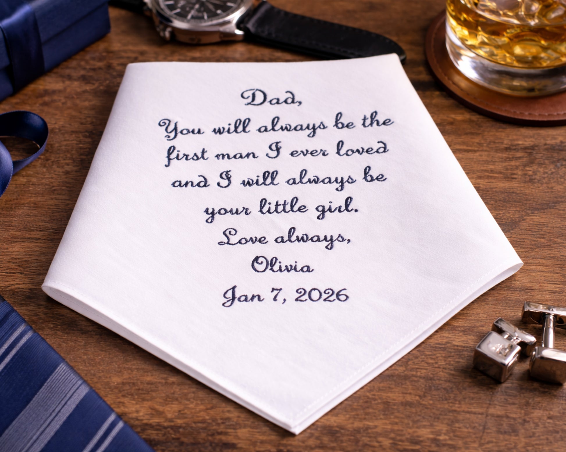 Personalized handkerchief with a message to a father on a wooden surface with a glass of whiskey.