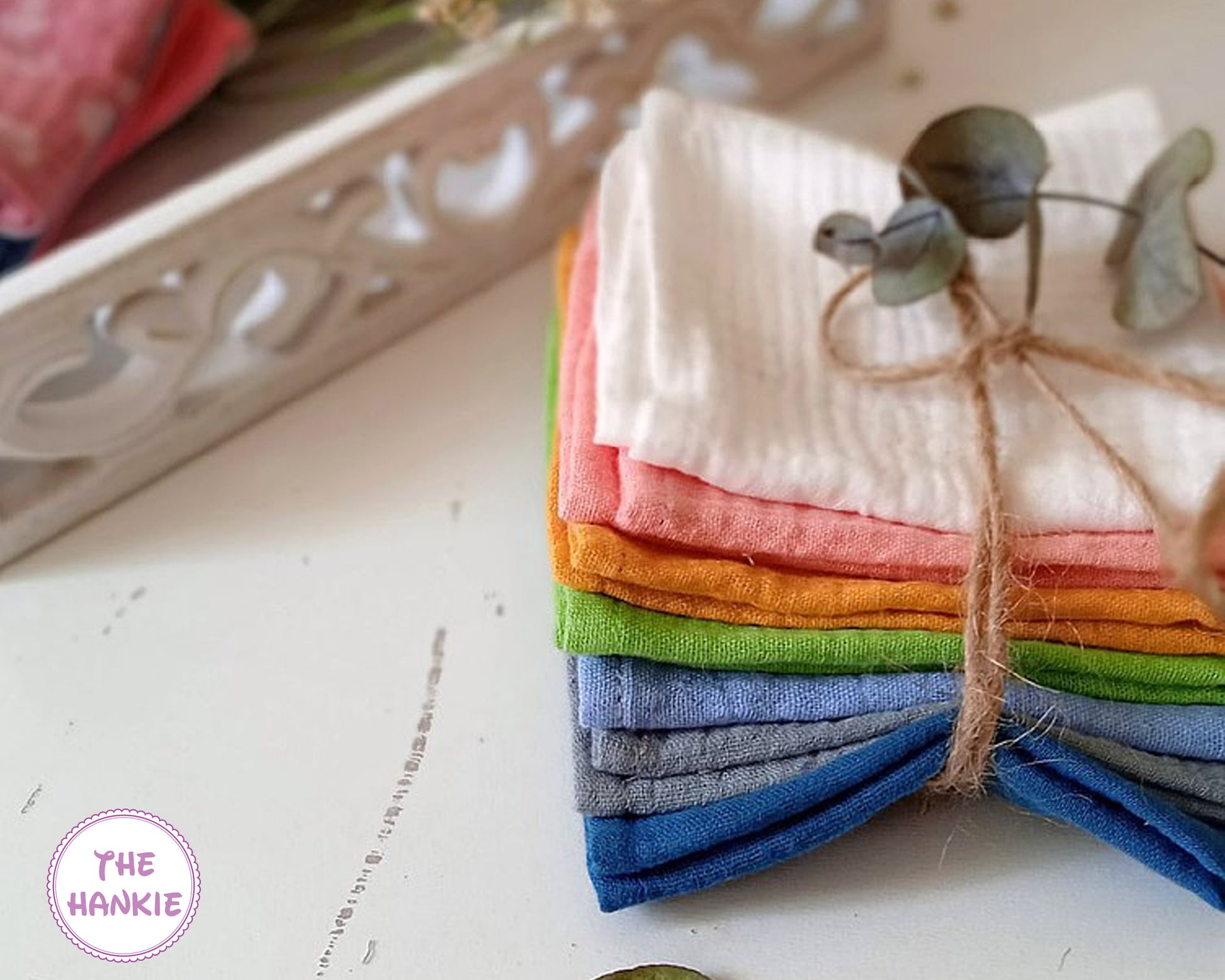 Stack of colorful hankies tied with twine on a textured surface, with 'The Hankie' brand visible.