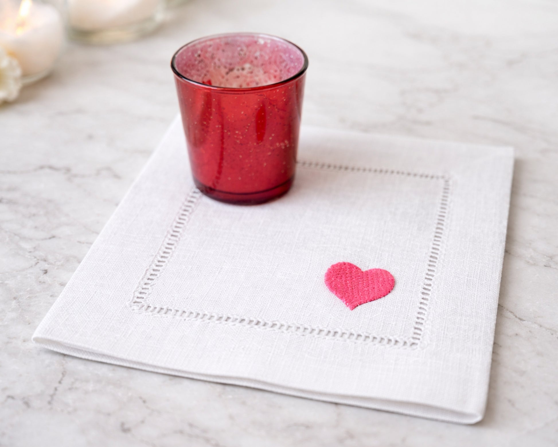 Red glass on a white napkin with a pink heart design on a marble surface