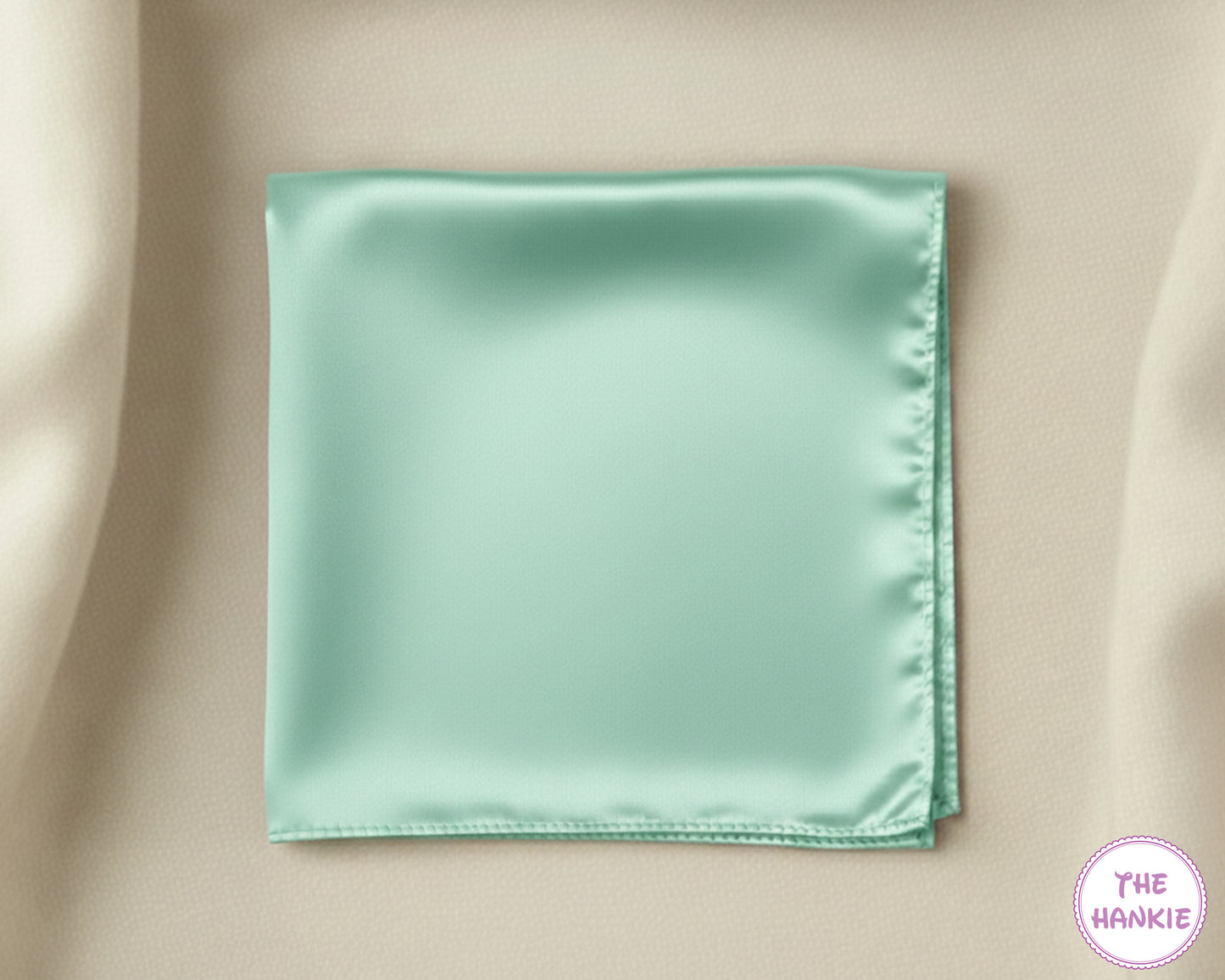 Mint green satin pocket square on a beige fabric background