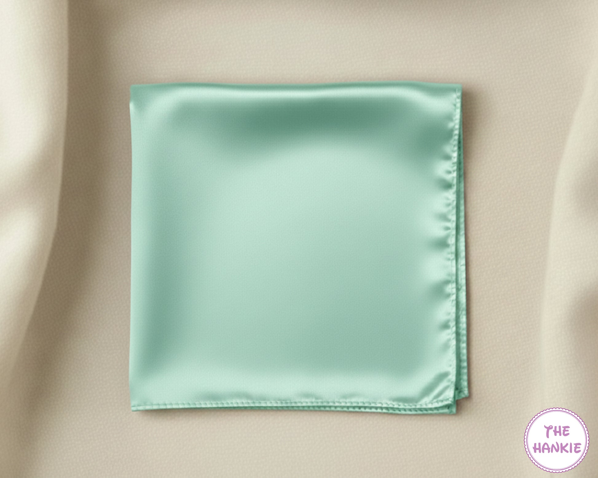 Mint green satin pocket square on a beige fabric background