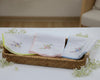 Set of embroidered handkerchiefs in a woven basket on a white surface with flowers.