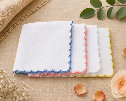 Set of four folded handkerchiefs with scalloped edges in blue, pink, and white on a beige fabric background.