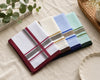 Set of four striped handkerchiefs on a beige surface with a plant and book in the background.