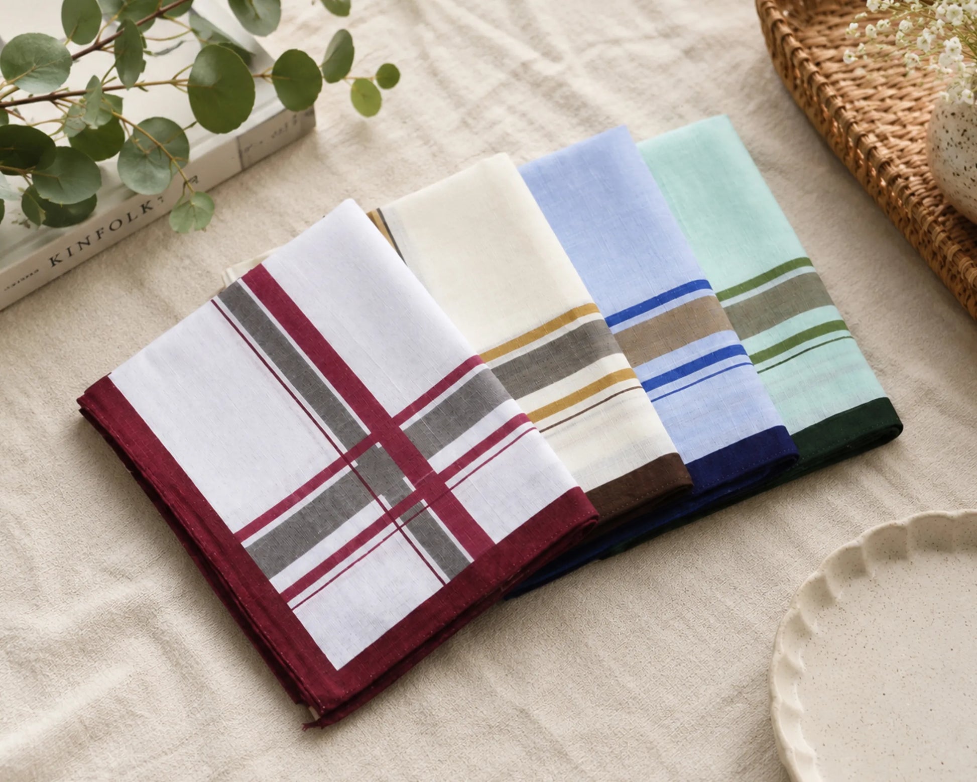 Set of four striped handkerchiefs on a beige surface with a plant and book in the background.
