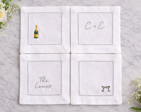 Set of four white napkins with personalized designs on a marble surface.