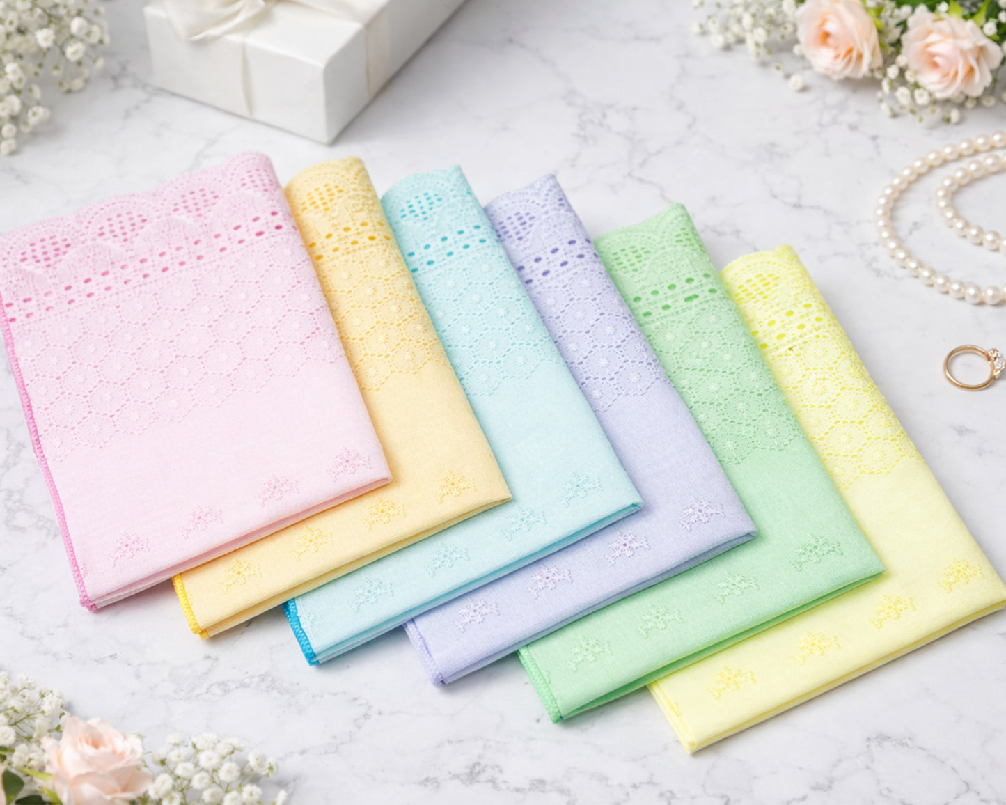 Set of pastel-colored handkerchiefs on a light surface with flowers and jewelry in the background.