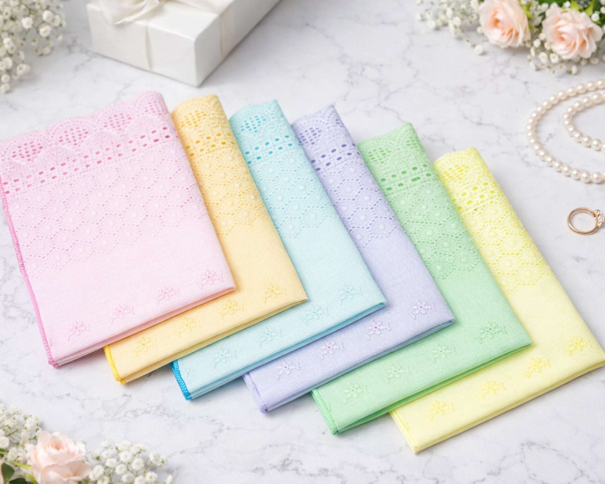 Set of pastel-colored handkerchiefs on a light surface with flowers and jewelry in the background.